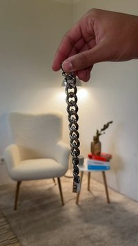 Srebrna bransoletka z łańcuszka z metalowymi, połączonymi ze sobą ogniwami. Gładka tekstura z bezpiecznym zapięciem; trzymana w dłoni na neutralnym tle.