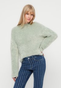 Minzgrüner, flauschiger Pullover mit hohem Kragen, langen Ärmeln und lockerer Passform, kombiniert mit blau gestreiften, hoch taillierten Jeans.