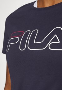 Námořnické bavlněné tričko s výrazným bílým a červeným logem "FILA". Krátké rukávy, kulatý výstřih, hladká textura a volný střih.