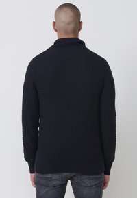 Handgestrickter navyfarbener Pullover mit hohem Kragen, geripptem Muster und langen Ärmeln. Hat eine lässige Passform sowie kontrastierende Bündchen und Saum.