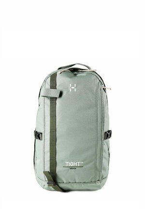 Zaino verde di media dimensione con cinturino verticale anteriore, fibbie laterali, maniglia superiore e la scritta "TIGHT™ MEDIUM" stampata sul davanti.