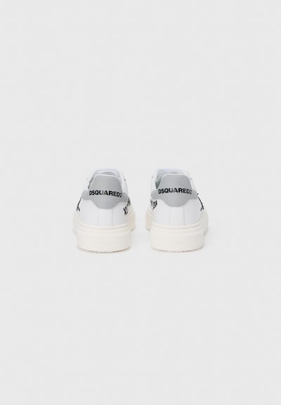 Baskets en cuir blanc avec languettes de talon grises, texte de logo noir et semelles en caoutchouc texturées. Design minimaliste avec une silhouette épurée et moderne.