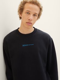 Čierna mikina vyrobená z mäkkej látky, na hrudi s modrým logom "DENIM TOM TAILOR". Pružný okrúhly výstrih a manžety.