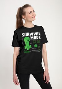 Czarny T-shirt z zielonym motywem Minecraft Creeper i napisem "TRYB PRZETRWANIA." Projekt zawiera kwadratowe tekstury i ikony związane z grą.