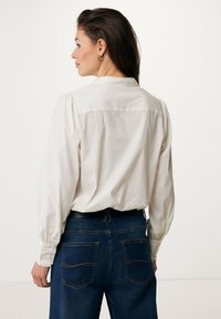 Witte lange mouwen shirt met een geplooide achterkant en knoopmanchetten, gecombineerd met donkerblauwe jeans met contrasterende stiksels en achterzakken.