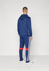 Navy hoodie and sweatpants set, featuring red and white side stripes. The fabric is smooth, with a fitted design and hood detail.