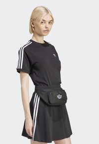 Svart t-skjorte med tre hvite striper på ermene, kombinert med en svart skjørt. Svart midjeveske med hvit logo. Enkel og sporty design.