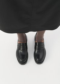 Μαύρα δερμάτινα λουστρίνια με στρογγυλή μύτη, που διαθέτουν μια διακοσμητική ζώνη μπροστά και υφασμένο καουτσούκ σόλα.