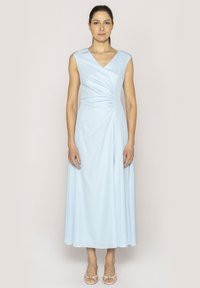 Jasnoniebieska sukienka bez rękawów z dekoltem w kształcie litery V, z drapowaną konstrukcją i marszczeniem w talii, sięgająca do długości midi. Pasujące sandały.