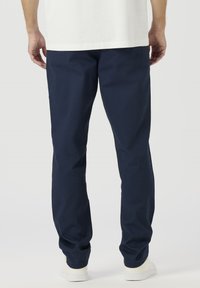 Tumši zili kokvilnas maisījuma bikses ar vaļēju piegriezumu, taisnām pēdām un elastīgu vidukļa joslu. Valdātas ar baltām sporta kurpēm.