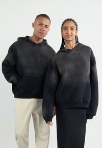 Sweat-shirts à capuche noirs surdimensionnés avec un effet dégradé, dotés de poches avant et de poignets côtelés. Texture douce et coupe décontractée.