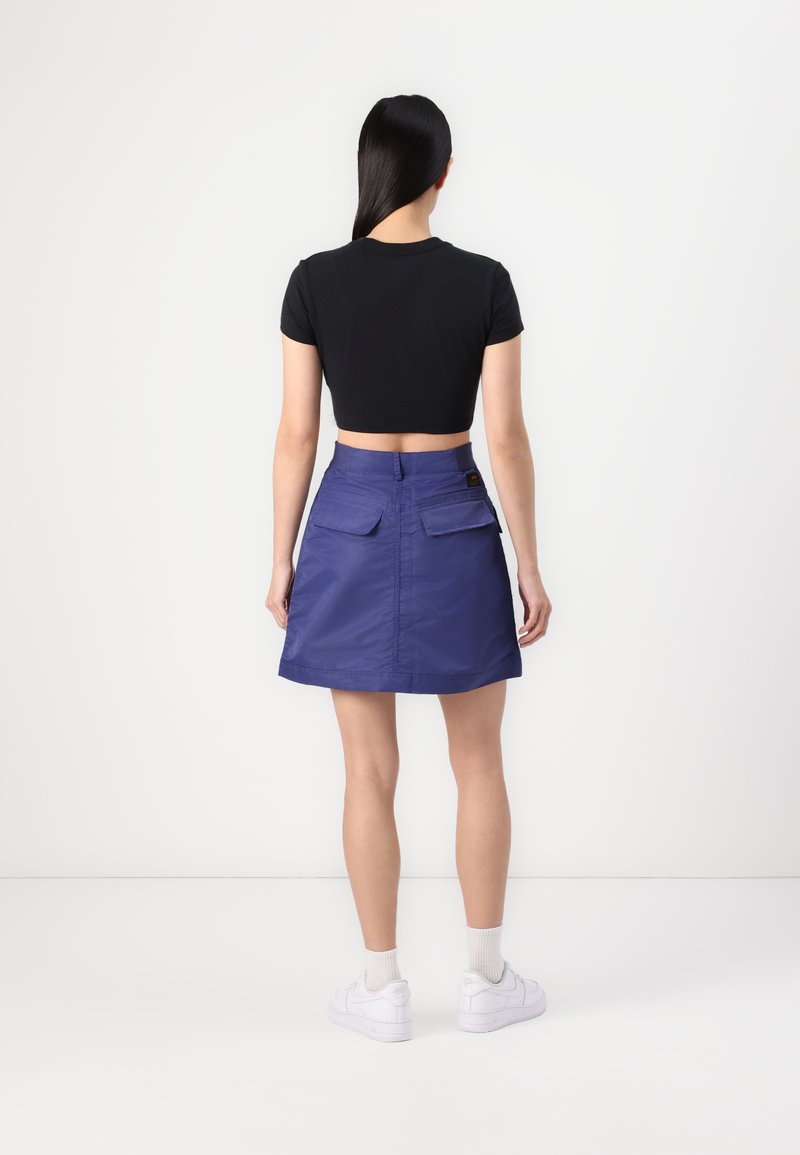 Cropped black t-shirt, purple skirt with two back pockets, smooth texture, a-line shape, paired with white sneakers and ankle socks.