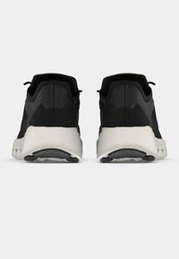 Chaussures de sport noires avec une tige texturée respirante, une semelle intermédiaire blanche contrastante et une semelle extérieure en caoutchouc, présentées en vue arrière.