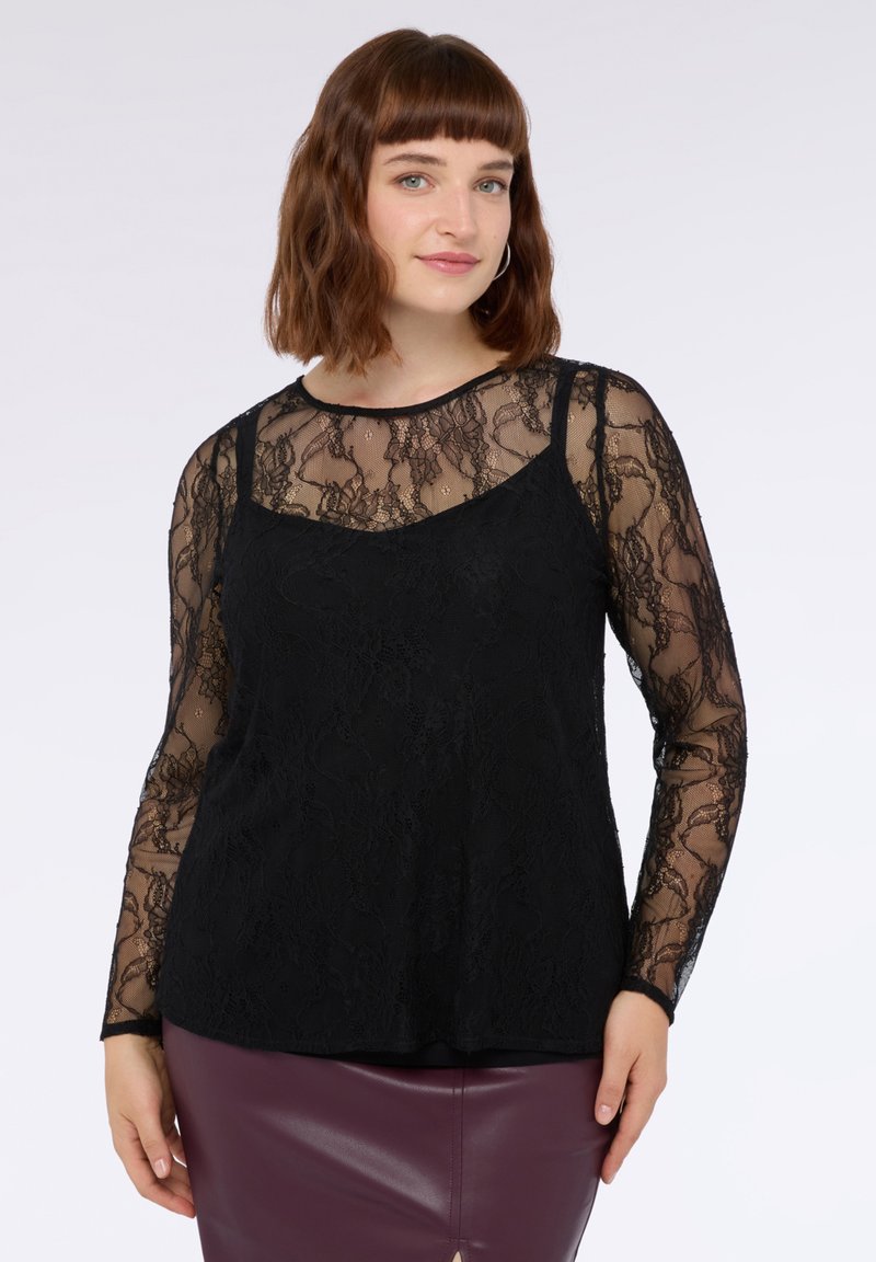 Top lungo a maniche in pizzo nero con sovrapposizione trasparente, scollatura rotonda e sottogusto aderente. Il design presenta motivi floreali.