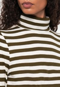 Strikkegenser med horisontale striper i olivengrønn og hvit. Stoffet ser mykt ut med en jevn tekstur. Ingen synlig maskinvare eller aksenter.