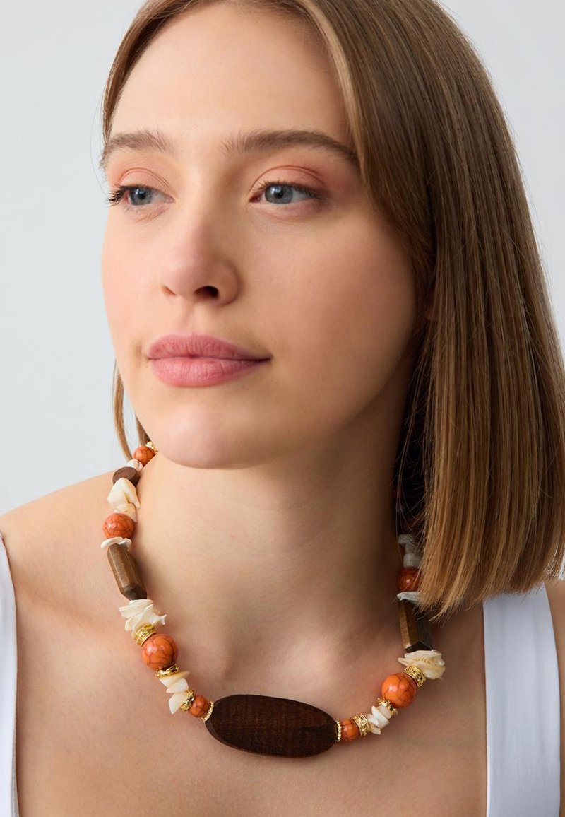 Kralenketting met houten en oranje gemarmerde kraaltjes, met witte schelpen accenten en gouden hardware. Getextureerde, natuurlijke materialen.