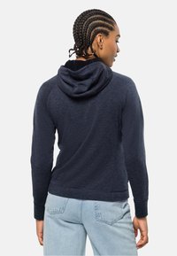 Felpa blu navy con una texture morbida, dotata di cappuccio con cordino e maniche raglan. Abbinata a jeans in denim chiaro.