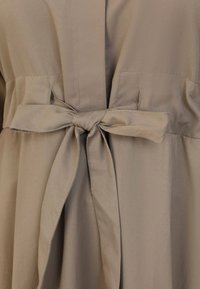 Beige jurk met een knooptaille, zachte stof en een gladde textuur. Het ontwerp bevat zakken en een vloeiende silhoeët.