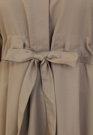 Vestido beige con cinturón en la cintura, fabricado en un tejido suave y de textura lisa. El diseño incluye bolsillos y una silueta fluida.