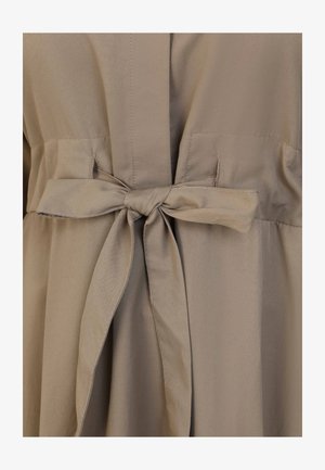 Robe beige avec une taille nouée, en tissu doux et avec une texture lisse. Le design comprend des poches et une silhouette fluide.
