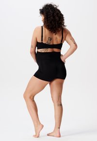 Svart sömlös underklädesset med en bralette med justerbara remmar och högmidjade shorts. Materialet har en slät, elastisk textur.