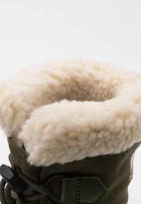 Stivale verde oliva con una morbida fodera in pelliccia sintetica color crema. Presenta un materiale esterno testurizzato e un sistema di lacci regolabile.