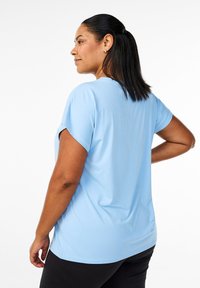 Light blue short-sleeve top with a round neckline, relaxed fit, and smooth texture, paired with black pants.