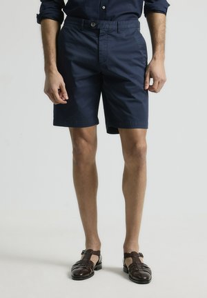 Shorts navy de tejido ligero, con cierre de botón y bolsillos laterales. Combinados con sandalias de cuero marrón trenzadas.