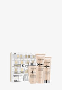 Set di prodotti per la cura dei capelli Kérastase Curl Manifesto in una scatola illustrata bianca e dorata, con uno shampoo con coperchio argentato e due tubi beige.