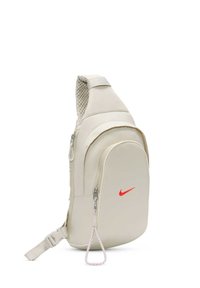 Beige slinga ryggsäck med en enda vadderad axelrem, med en röd Nike-logotyp, dragkedjefack och en texturerad bakpanel.