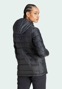 Svart puffjacka med huva, med horisontella quiltade sektioner, en mjuk yta och figurnära design. Lämplig för utomhusbruk.