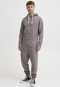 Gray zippered onesie with a hood, contrasting cream drawstrings, front pockets, and ribbed cuffs, paired with black sneakers.
