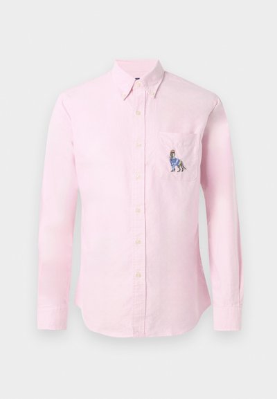 Chemise à manches longues rose clair avec un col boutonné et un design de chien brodé sur la poche poitrine gauche. Tissu en coton, texture lisse.