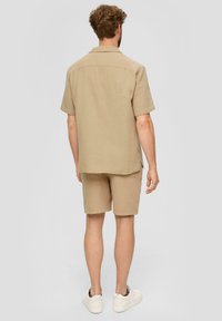 Beige shirt met korte mouwen en bijpassende shorts van textuurstof. Casual ontwerp met een rechte zoom, gedragen met witte sneakers.