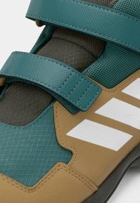Teal and brown sports shoe with a textured upper, two teal velcro straps, and three white stripes on the side.