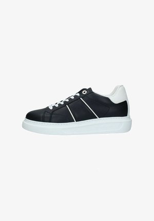 Zapatilla negra de perfil bajo con suela blanca, cordones blancos y cuello blanco en el talón, con delgadas rayas diagonales blancas en el lateral.