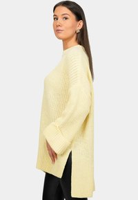 Maglione giallo a maglia con una vestibilità ampia, texture spessa, spacchi laterali e maniche lunghe. Presenta polsi a coste e un ampio scollo.