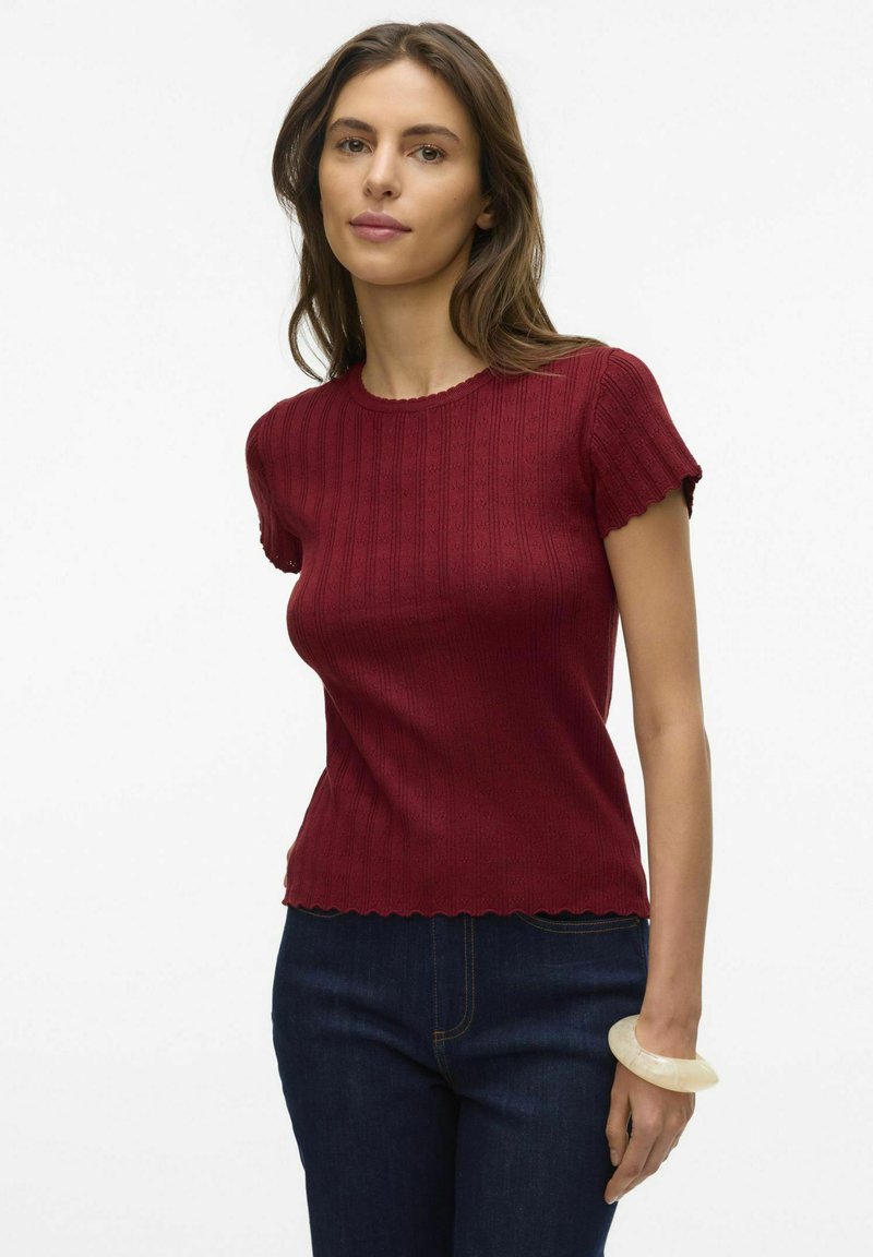 Haut court à manches courtes en tricot ribbed rouge avec des bords scallopés et un col ras du cou, associé à un jean en denim foncé.