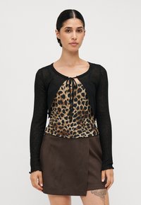 Crna kardigan jakna dugih rukava s vezanjem, složena preko majice s leopard printom, uparen s smešnim suknjom od umjetnog sueda s dijagonalnim preklopom.
