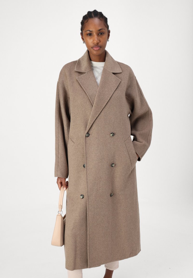 Brauner, doppelt geknöpfter Wollmantel mit großen Revers, Seitentaschen und grünen Knöpfen. Glatte Textur und übergroße Passform.