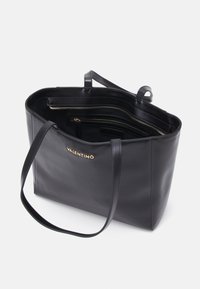 Svart läder tote-väska med två långa handtag, guld-logotypaccent och flera innerfickor. Slät textur med en rymlig design.