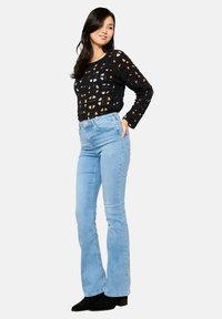 Suéter de punto negro con patrones recortados, combinado con jeans de campana de color azul claro. El modelo lleva botas negras hasta el tobillo.