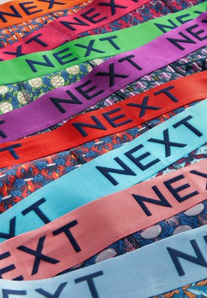 Bunte Stoffbänder, die jeweils den Text "NEXT" in Marineblau enthalten. Die Muster umfassen Hummer und florale Designs mit lebhaften Farben wie Rot, Lila und Blau.