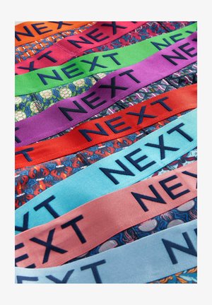 Des bandes de tissu colorées, chacune arborant le texte "NEXT" en marine. Les motifs incluent des homards et des designs floraux, avec des couleurs vibrantes comme le rouge, le violet et le bleu.