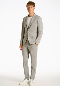 Traje gris claro de tela suave, ajuste entallado con blazer de un solo botón y pantalones de frente plano. Combinado con deportivas blancas.