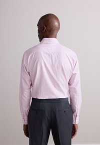 Heleroosa triibuline särk terava krae, pikkade varrukate ja nööpidega mansettidega, kombineeritud tumehallide rätsepatööna valminud pükstega.