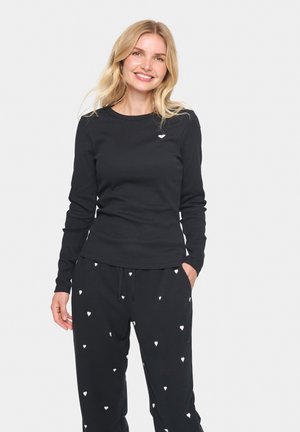 Black long-sleeve top with a ribbed texture and small white heart detail on the chest, paired with black pants featuring white heart patterns.