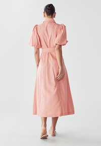 Duga ružičasta haljina od laganog materijala, s napuhanim rukavima, ovratnikom i pojasom na vezanje. Suknja seže do članaka.