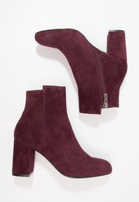 Paire de bottines en suède bordeaux pour femmes avec talons carrés et fermetures éclair sur les côtés, sur fond blanc.