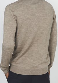 Jasnobrązowy dzianinowy sweter z zaokrąglonym dekoltem, długimi rękawami i prążkowanym wykończeniem na dole. Materiał wydaje się miękki i lekko teksturowany.